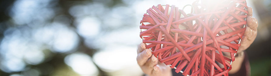 Basket material woven into a red heart with hands holding it